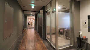 Un couloir doté d’un plancher en bois, de portes en verre et d’une petite table sur laquelle se trouvent une poubelle et une machine à café.