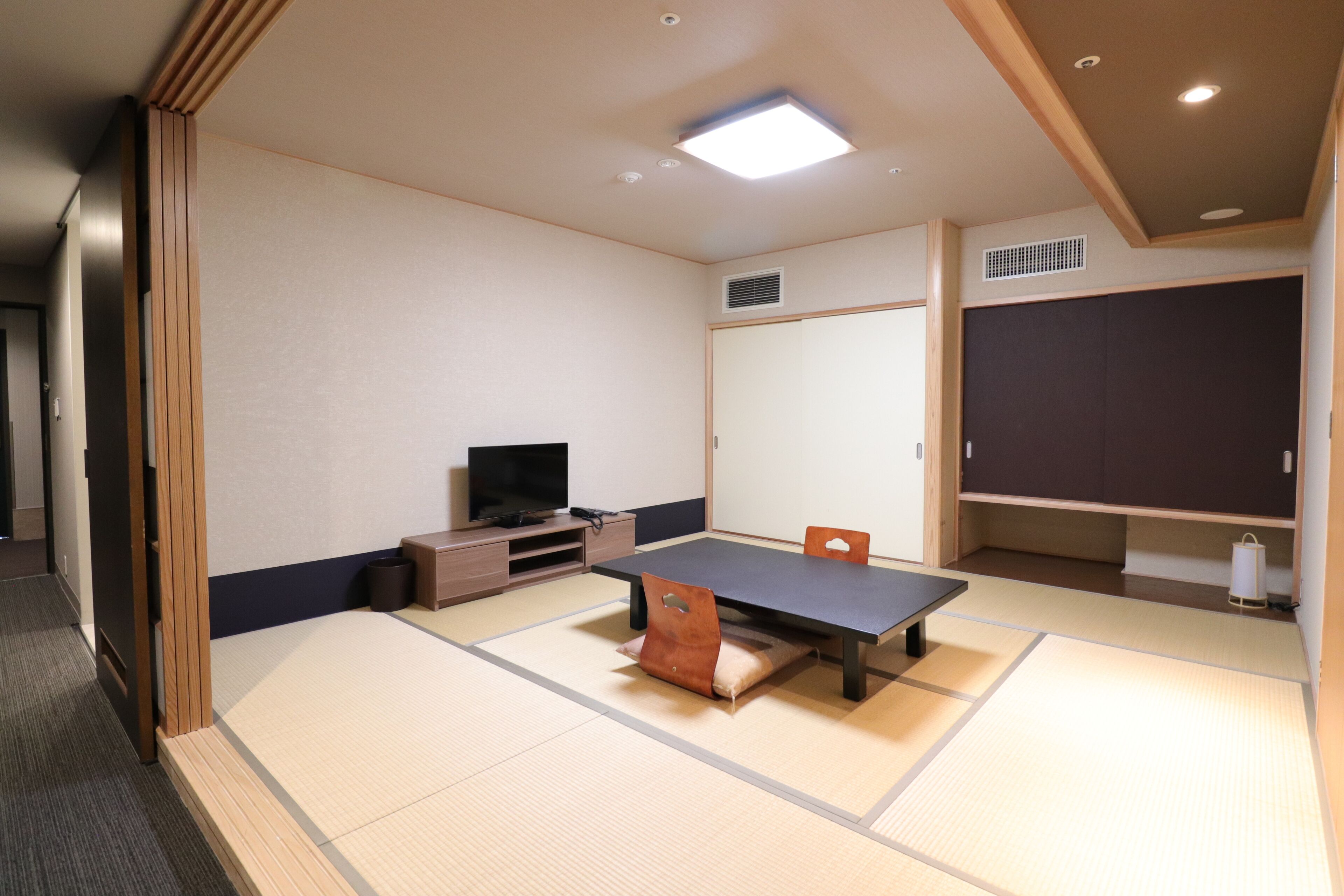 Una habitación con suelo de tatami, una mesa, un televisor y armarios de almacenamiento.