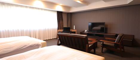 A hotel room with two beds, a desk with a chair, a television, and a window with curtains.