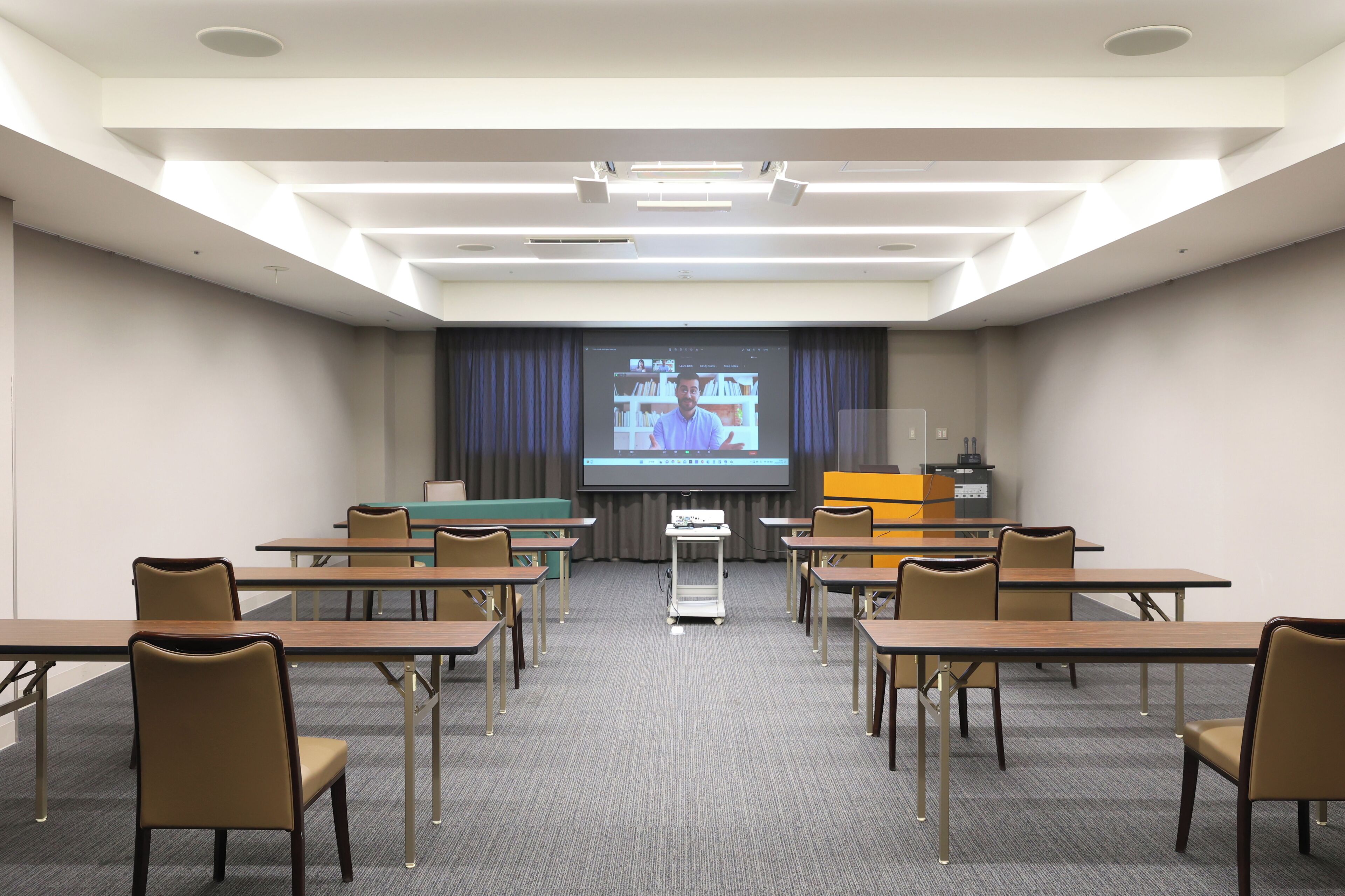 A conference room with tables, chairs, a projector screen, and a presentation.