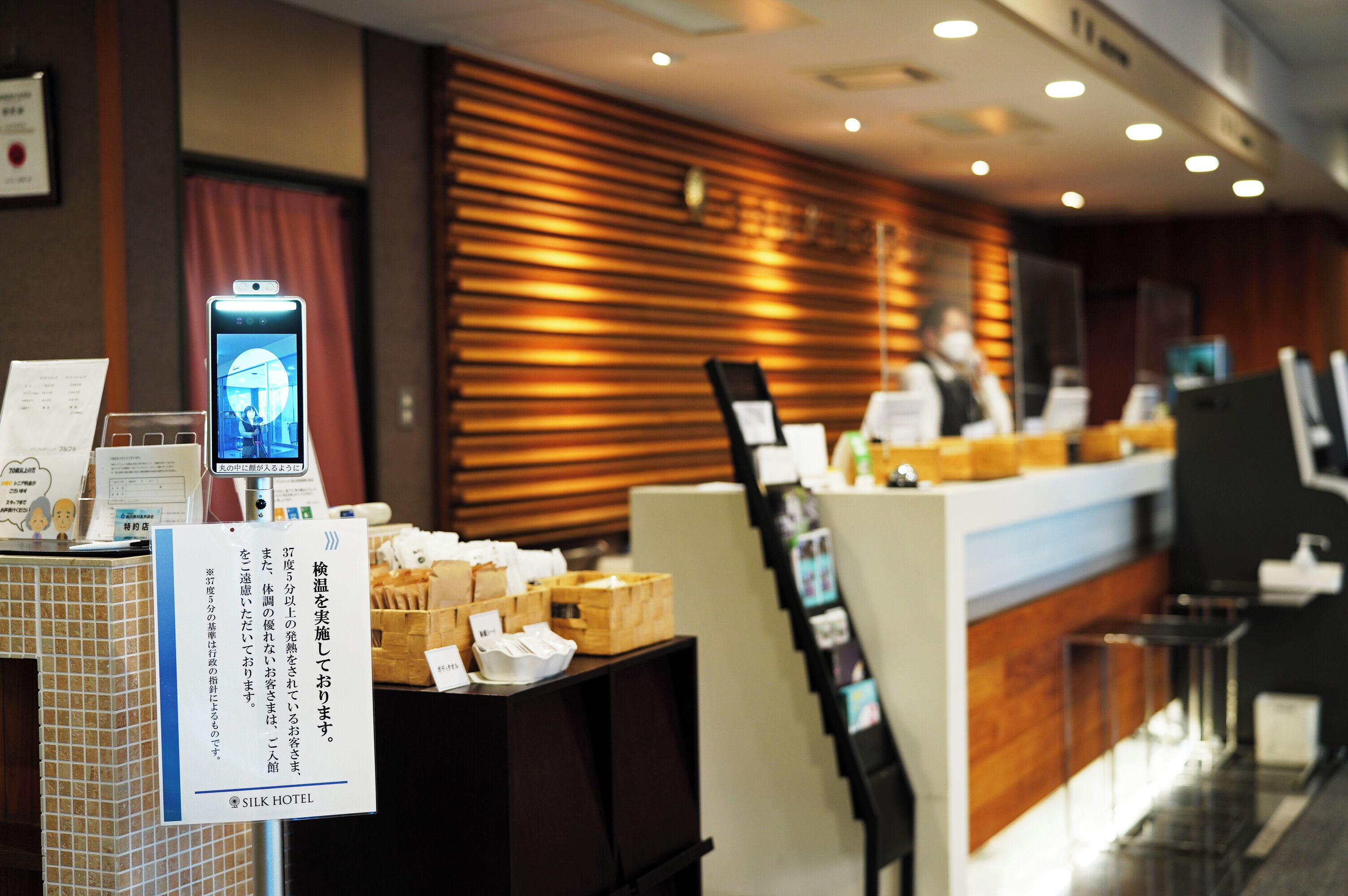 Un espace d’accueil d’hôtel avec un mur en bois, un comptoir doté d’un téléphone et un panneau affichant du texte en japonais.