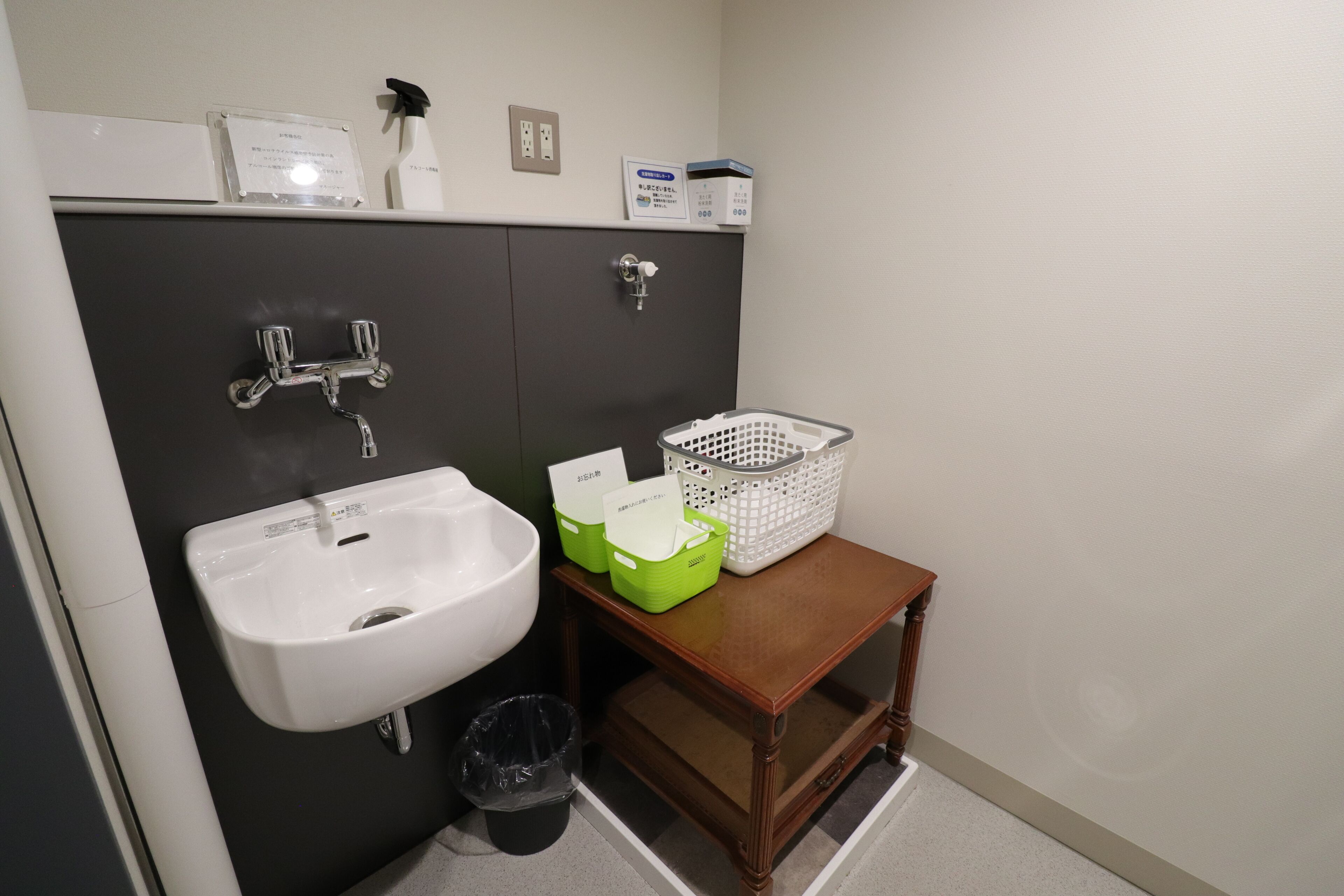 A bathroom with a sink, a mirror, a cabinet, a trash bin, and a small wooden table with baskets.