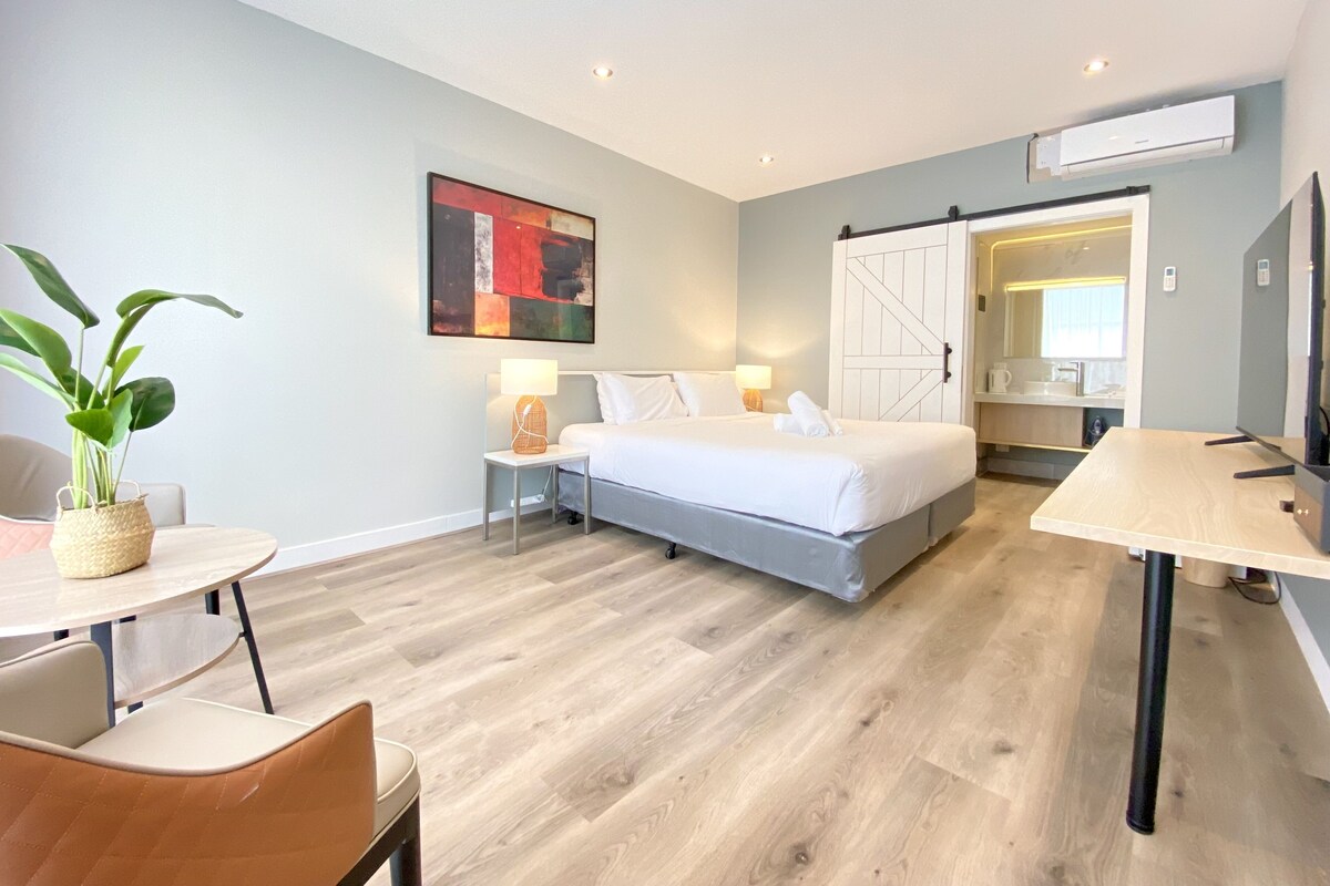 Quarto de hotel moderno com cama, mesas de cabeceira, escrivaninha e uma cadeira.