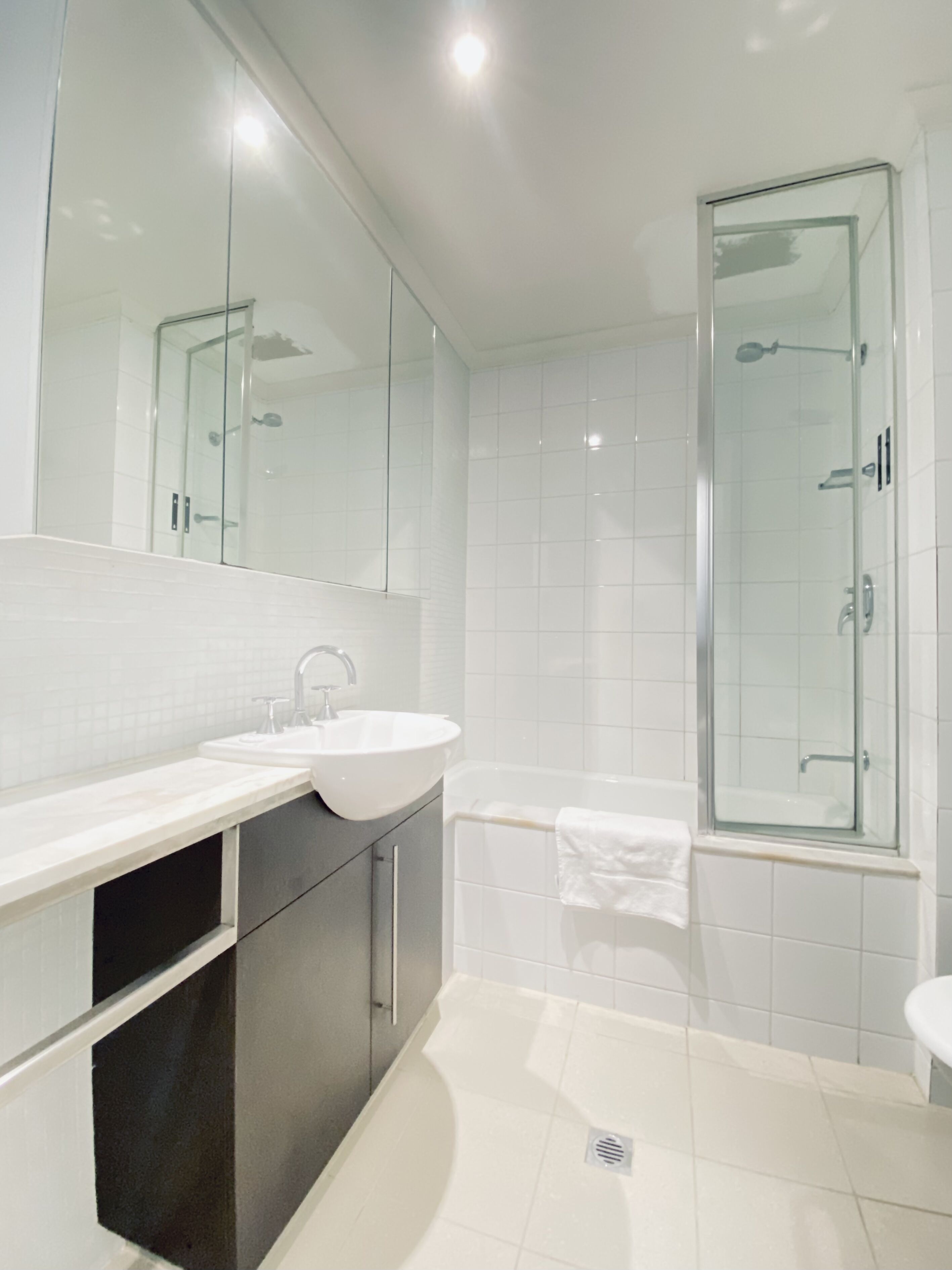 A modern bathroom with a large mirror, two sinks, a bathtub, and a glass-enclosed shower.
