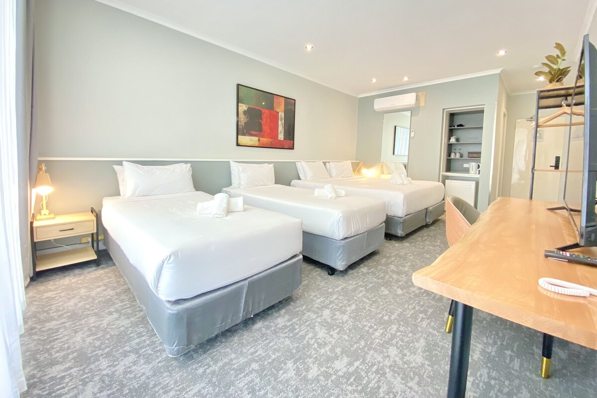 Quarto de hotel com duas camas, uma escrivaninha e um espelho.
