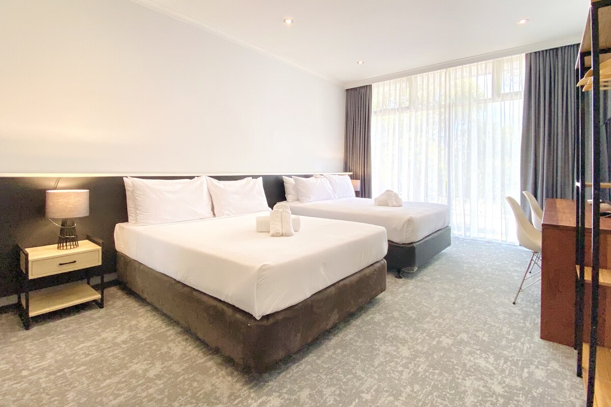 Quarto de hotel com duas camas, uma escrivaninha e uma cadeira.
