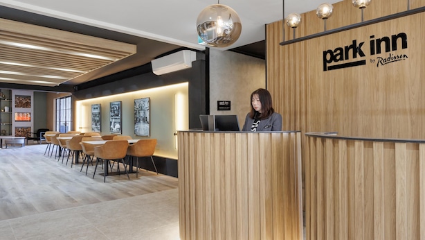 Zona de recepción con mostrador de madera, una recepcionista y un área de asientos con sillas.