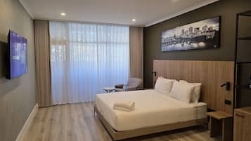 Un hotel moderno con una cama grande, una mesita, una silla y un cuadro de un paisaje urbano en la pared.