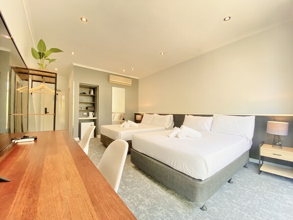 Una habitación de hotel moderna con dos camas, un escritorio de madera, un espejo y una planta.