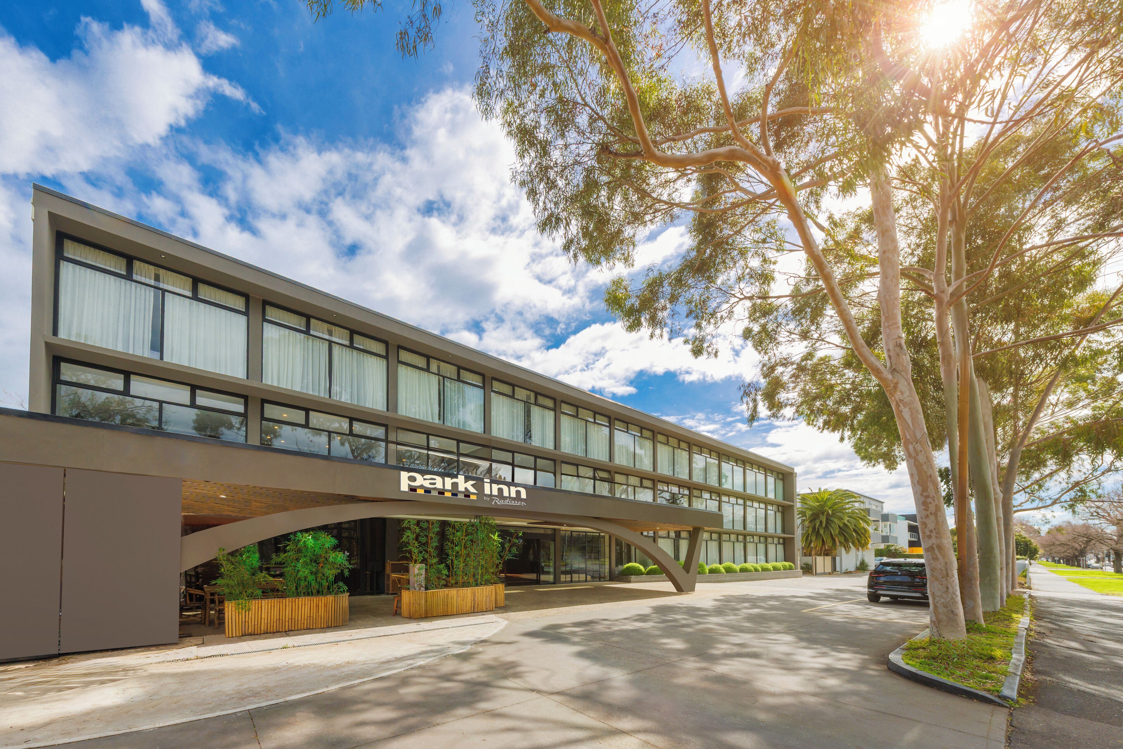 A modern building with a 'park inn' sign, featuring a covered walkway and a parking area.