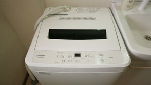A front-loading washing machine with a control panel, a power cord, and a nearby sink. - goom Hotel Nakasu (Fukuoka)