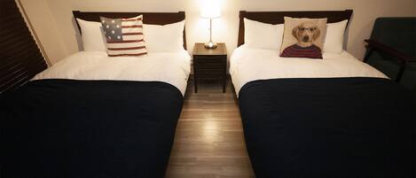 Two twin beds with a nightstand between them, each bed has a pillow with a dog design, and a lamp on the nightstand.