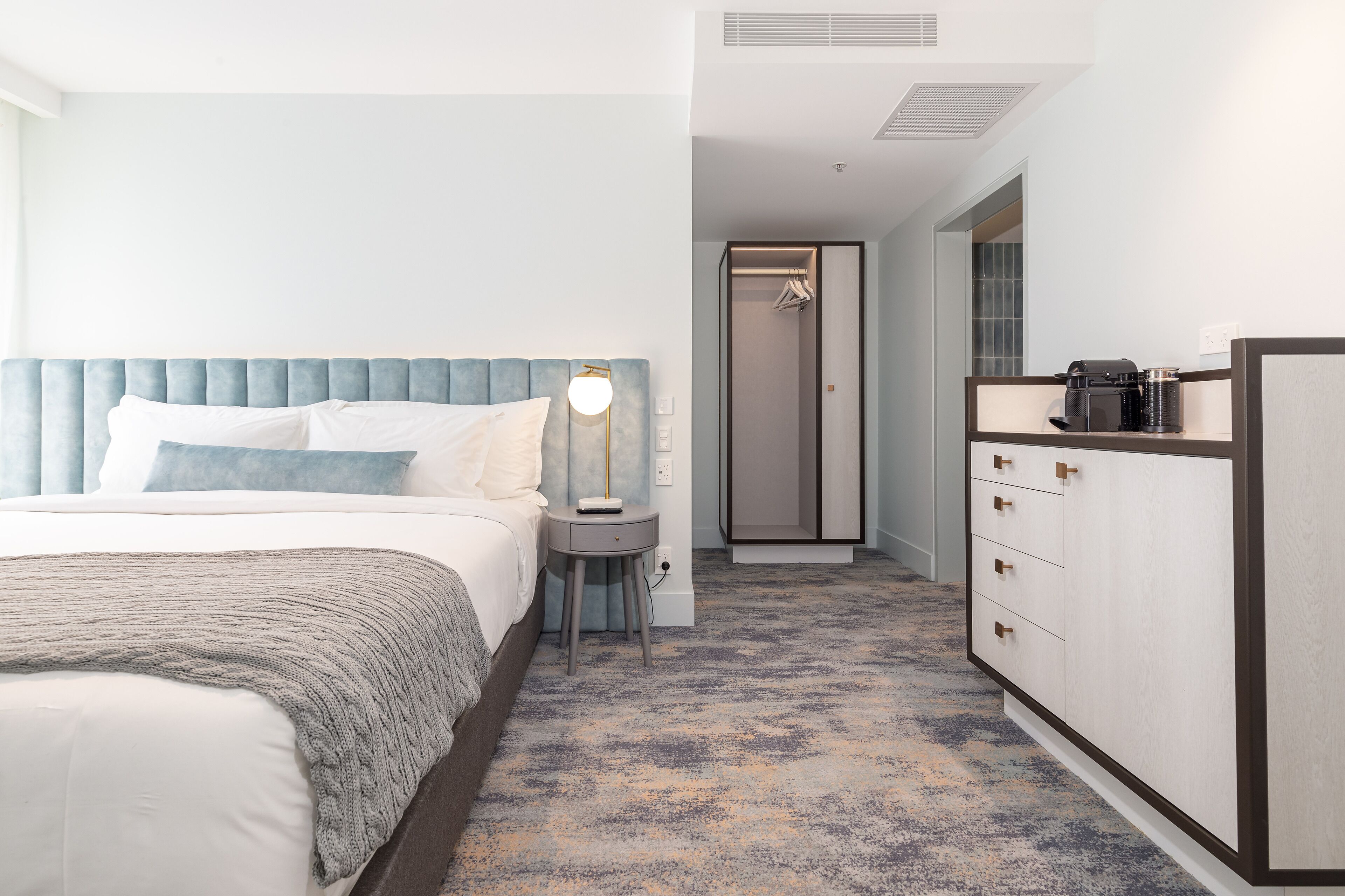 Una habitación de hotel con cama, mesita de noche, lámpara y armario.