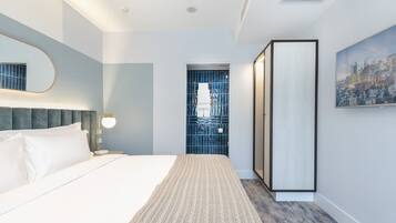 Una habitación de hotel moderna con una cama grande, una mesita de noche, un espejo montado en la pared, un cuadro de paisaje urbano y vistas de la ciudad a través de una ventana.