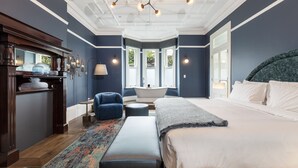 A bedroom with a large bed, a blue armchair, a bathtub, and a wooden dresser. - The Albert Hotel Mosman (Mosman)