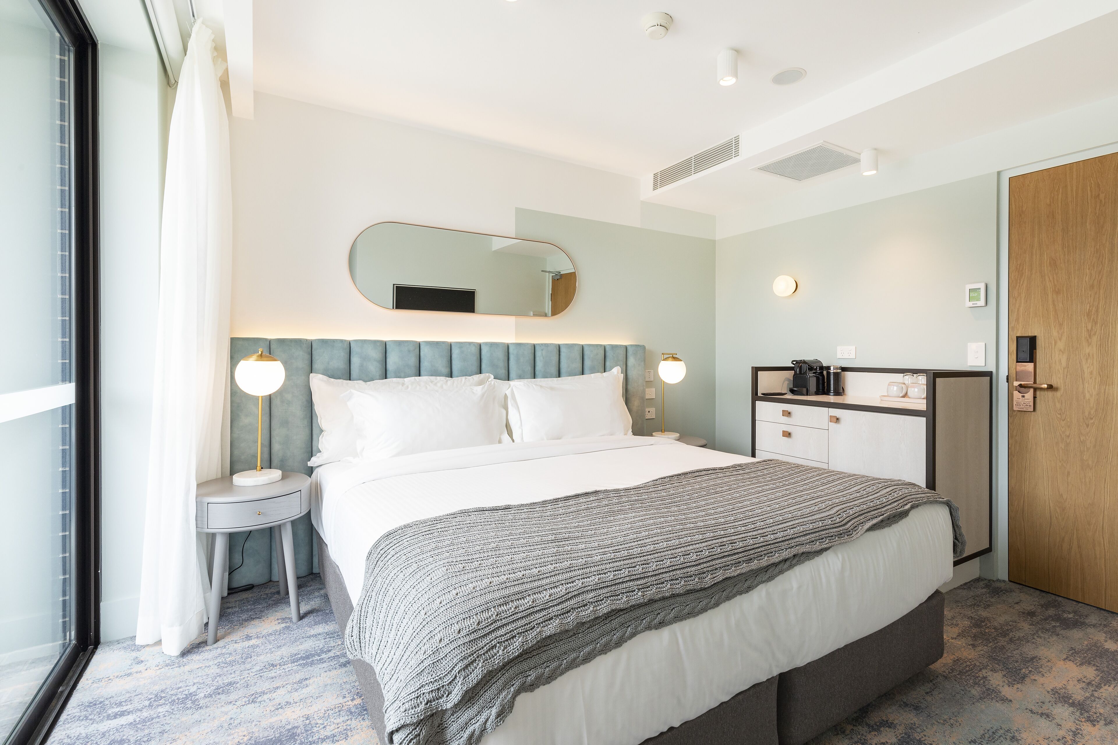 Ein modernes Hotelzimmer mit einem großen Bett, Nachttischen, einem Spiegel, einem Kleiderschrank und einer kleinen Küchenzeile.