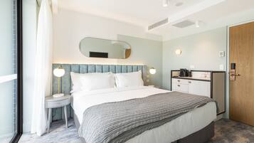Ein modernes Hotelzimmer mit einem großen Bett, Nachttischen, einem Spiegel, einem Kleiderschrank und einer kleinen Küchenzeile.