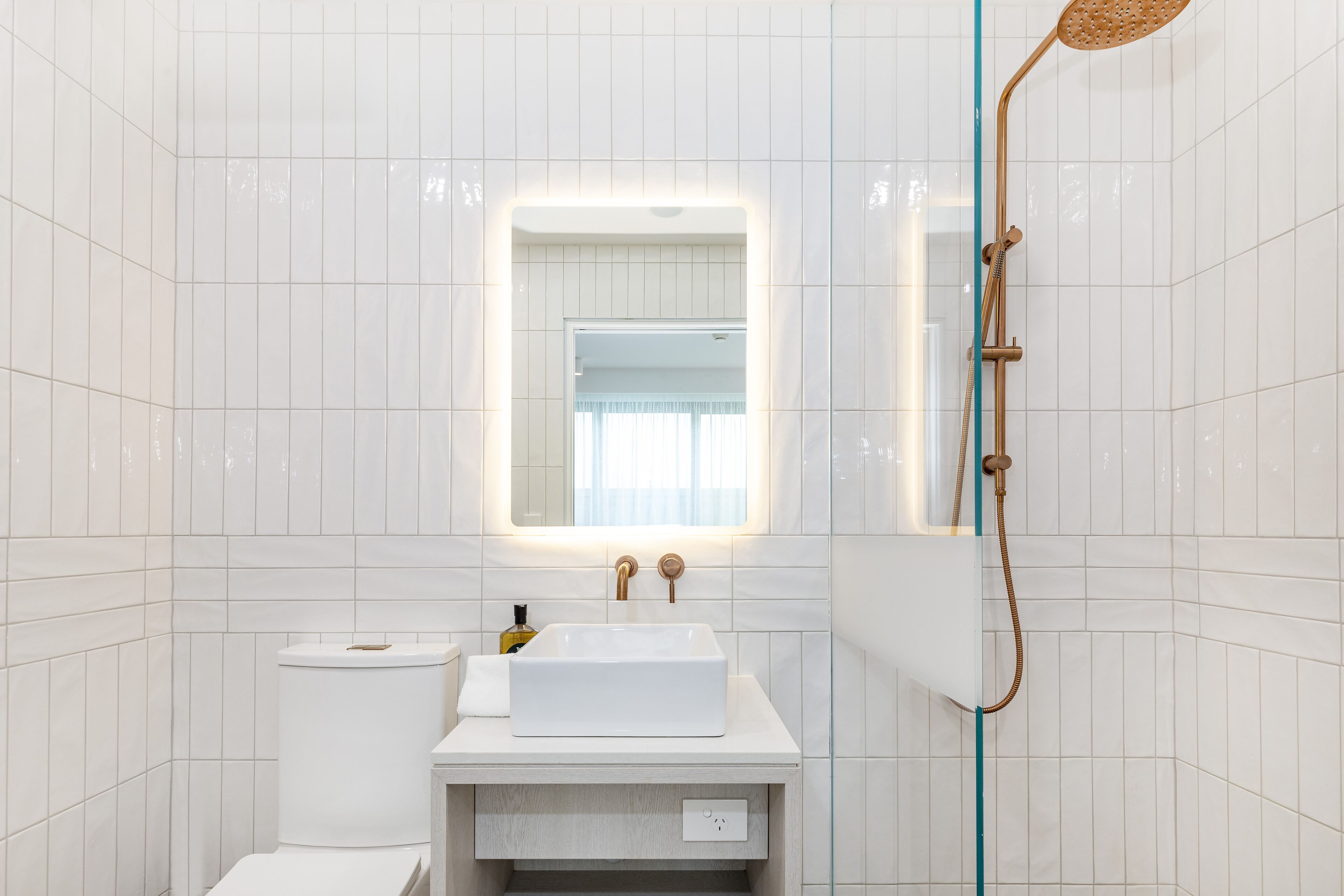 A modern bathroom with white tiles, a white sink, a mirror, and a shower.