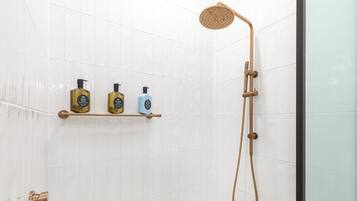 Un espace douche équipé d’un pommeau de douche à main et d’un robinet mural. Trois bouteilles sont posées sur une étagère au-dessus de la douche.