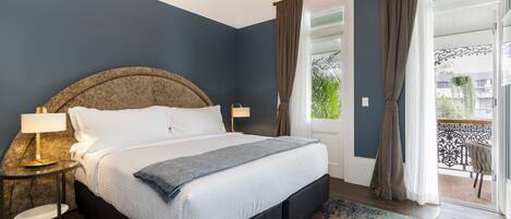 A bedroom with a large bed, a bedside table with a lamp, and a view of the outside balcony.