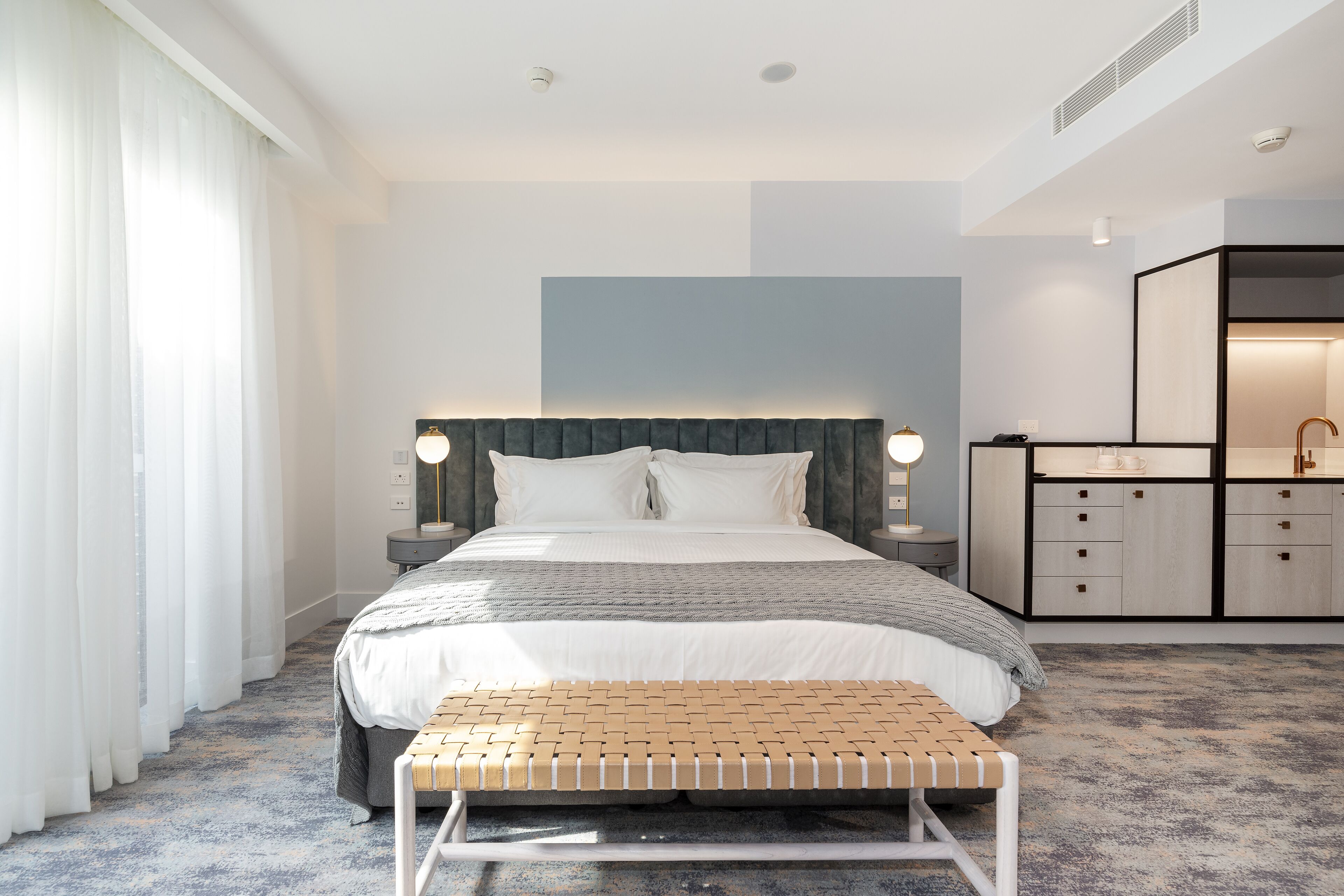 Una habitación de hotel moderna con una cama grande, mesitas de noche, un banco y un armario empotrado.