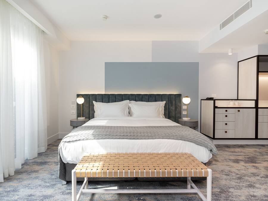 Una habitación de hotel moderna con una cama grande, mesitas de noche, un banco y un armario empotrado.