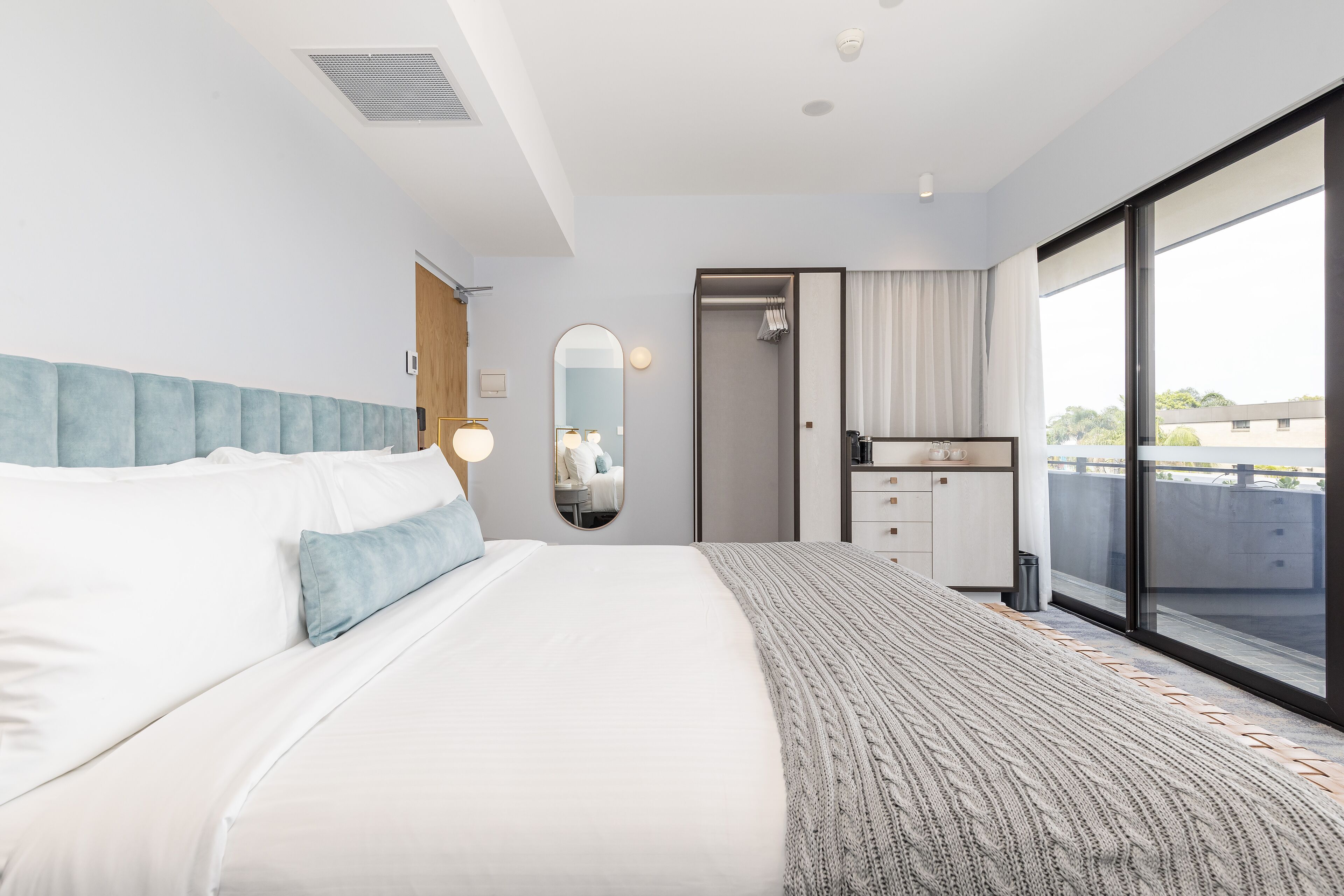 A modern hotel room with a large bed, a bathroom with a shower, and a view through a sliding glass door.