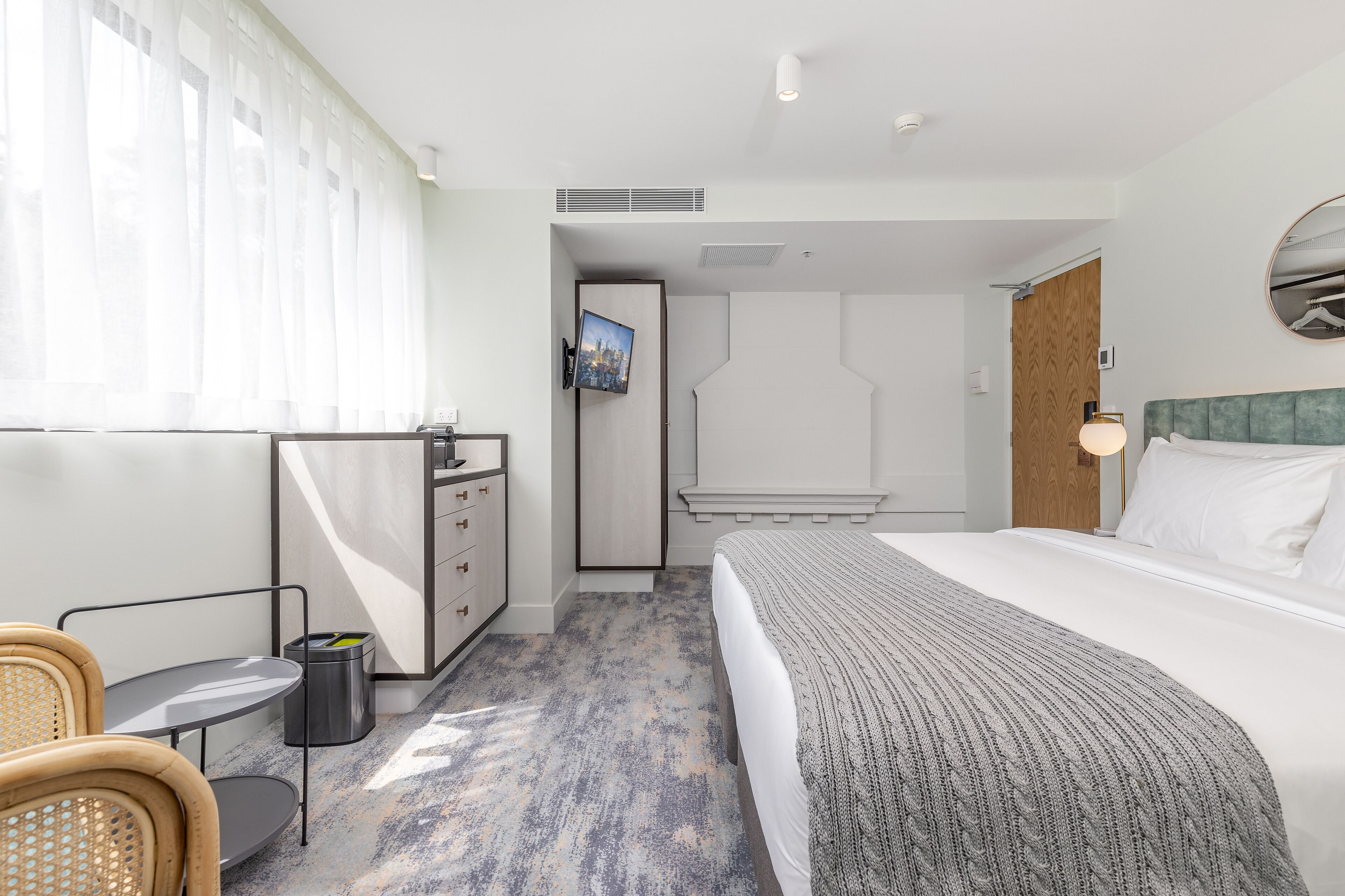 A hotel room with a bed, a desk, a chair, a trash bin, and a wardrobe.