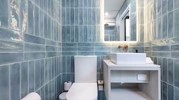 Ein Badezimmer mit blauen Fliesen, einer weißen Toilette, einem Waschbecken mit Spiegel und einem Handtuchspender.