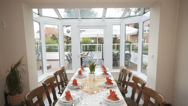 Un comedor con una mesa larga dispuesta para una comida, rodeada de sillas, y vistas al exterior a través de grandes ventanales.