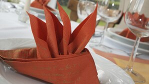 Una mise en place con un sujetapapeles rojo sobre un plato blanco, rodeado de copas de vino y un vaso de agua.