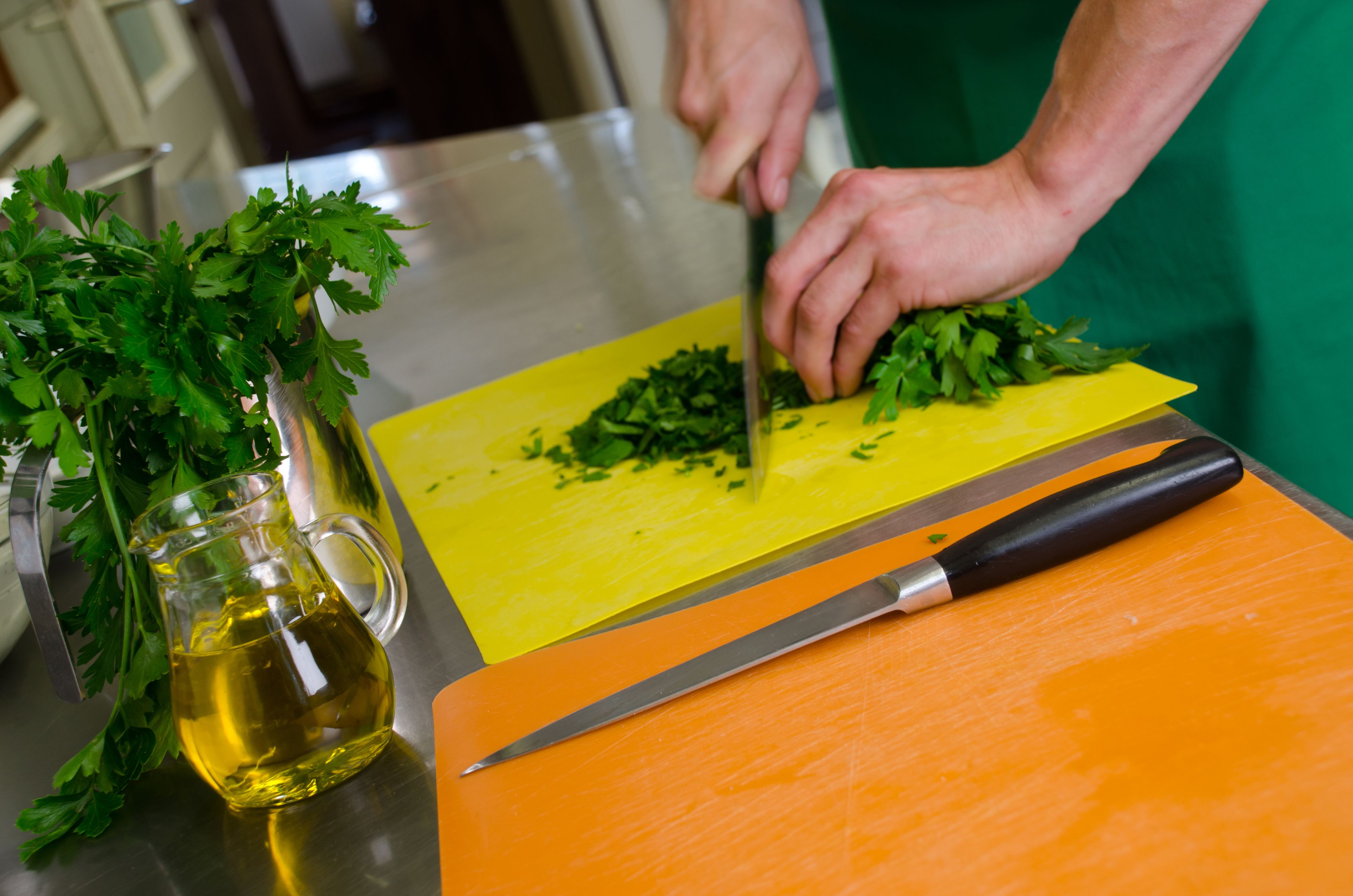 A person chopping parsley on a yellow cutting board with a knife.
