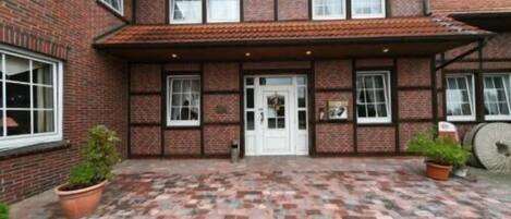 A two-story brick building with a tiled roof, a central white door, and multiple windows.