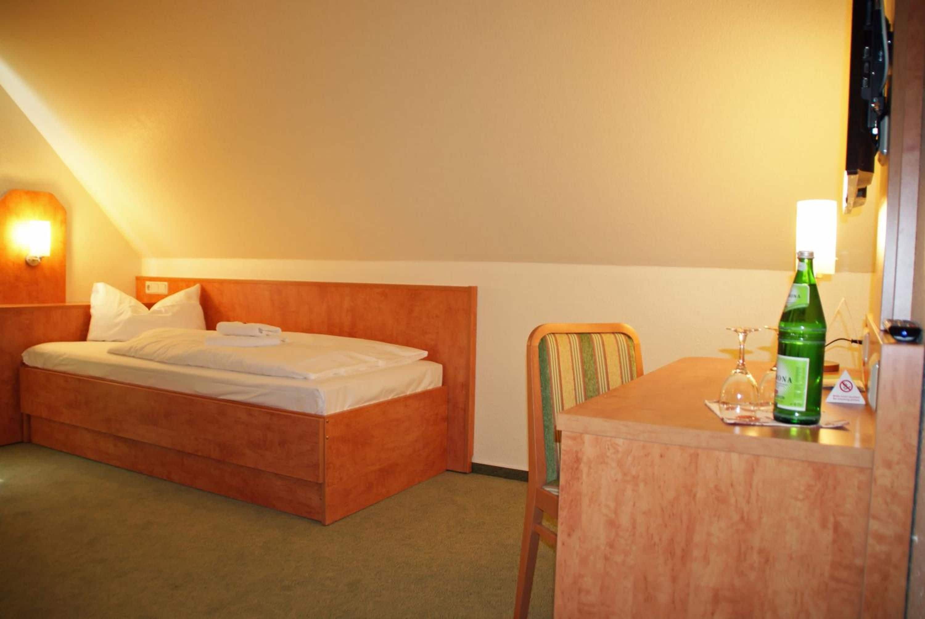 A hotel room with a bed, a chair, a table, and a bottle of water.