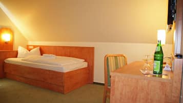 A hotel room with a bed, a chair, a table, and a bottle of water.