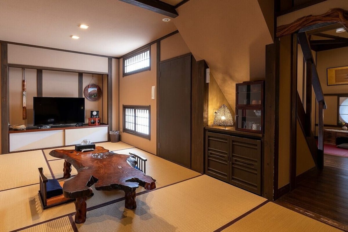 A traditional Japanese room with tatami flooring, a low wooden table, a television, and a sliding door.