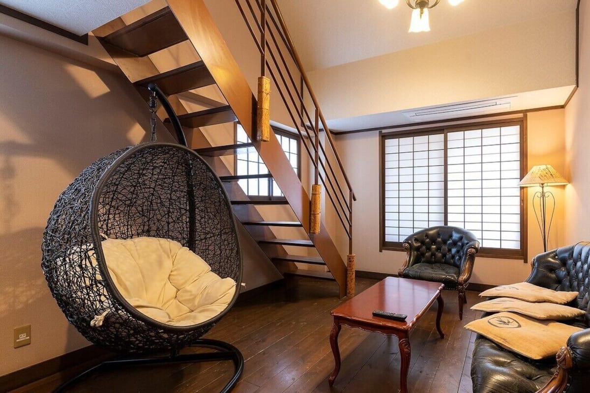 A room with a wooden staircase, a black rocking chair, a leather sofa, a small table, and a large window with a view.