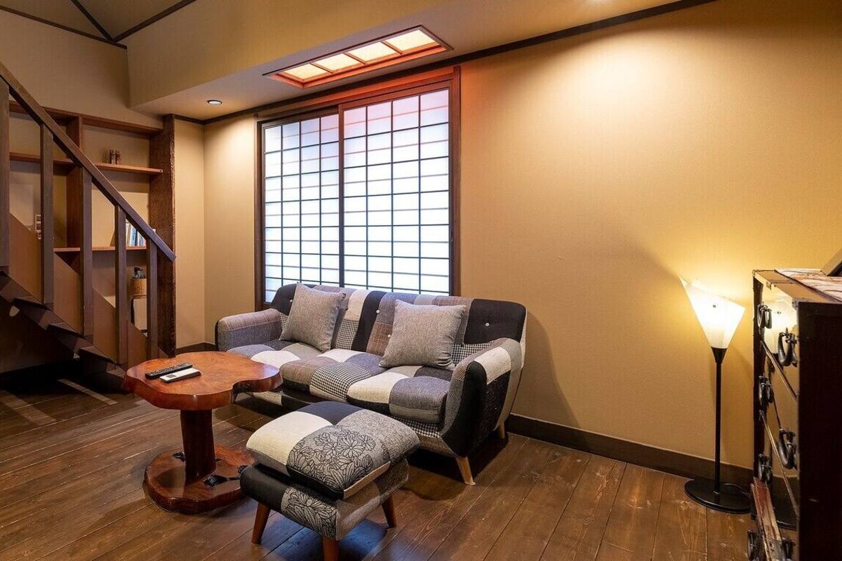 A room with a wooden staircase, a cushioned sofa, a small round table, and a large window with a grid pattern.