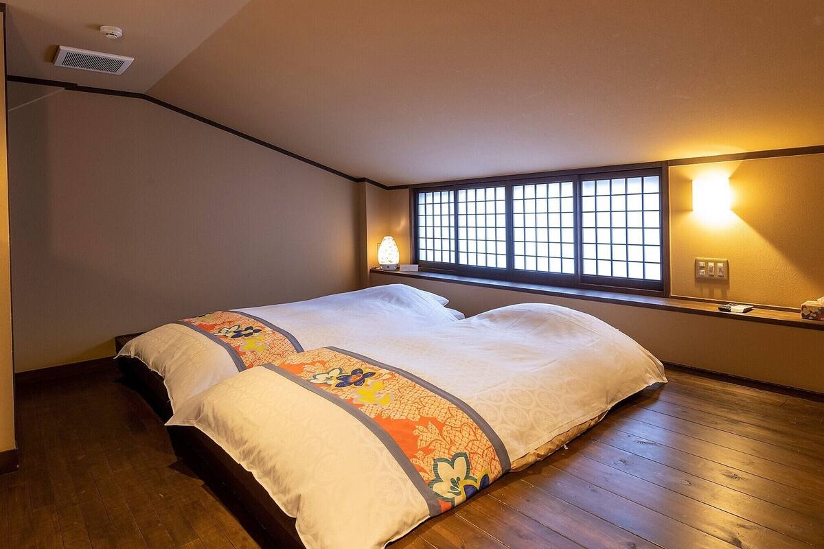 A room with a bed, a window with a view, a heater, and a wall-mounted lamp.