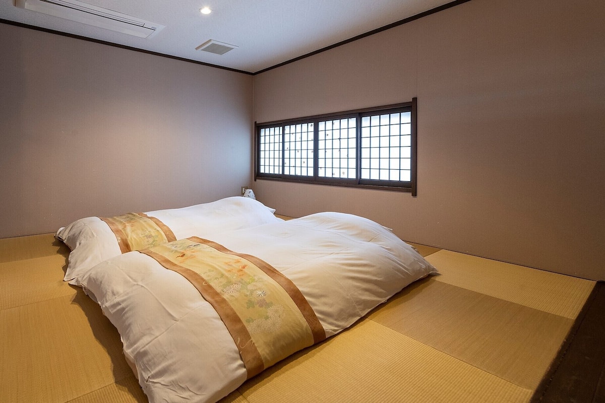 A room with tatami flooring, a bed with white bedding, a window with bars, and a sliding door.