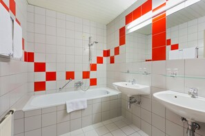 Un baño moderno con una bañera, dos lavamanos y un estante de vidrio.