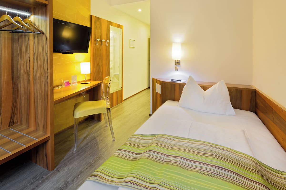 A hotel room with a bed, a desk, a chair, a TV, and a lamp.