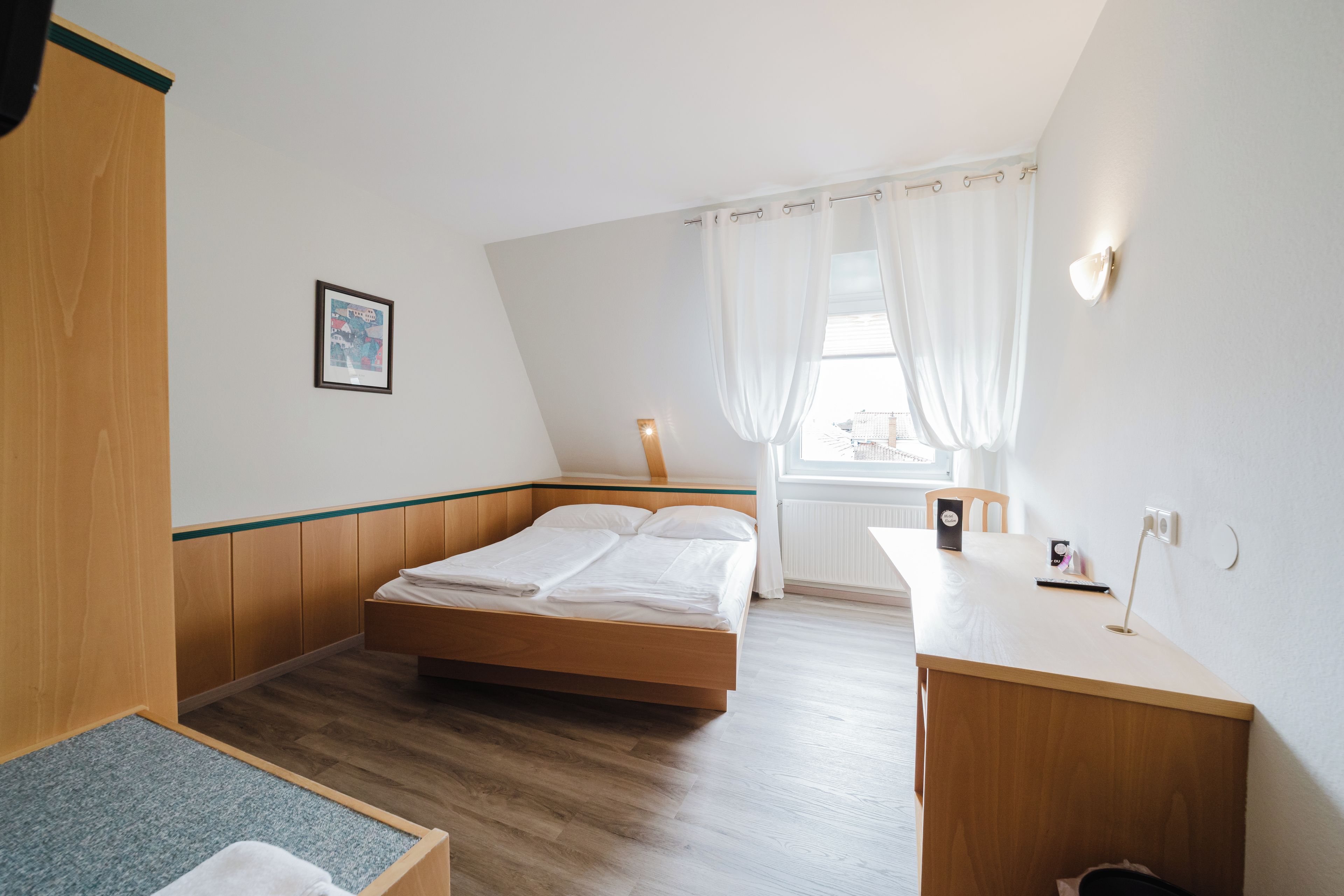Ein Schlafzimmer mit einem Holzbett, einem Schreibtisch und einem Fenster mit Vorhängen.