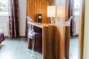 A room with a wooden table, two clear plastic chairs, a lamp, and a window with curtains.