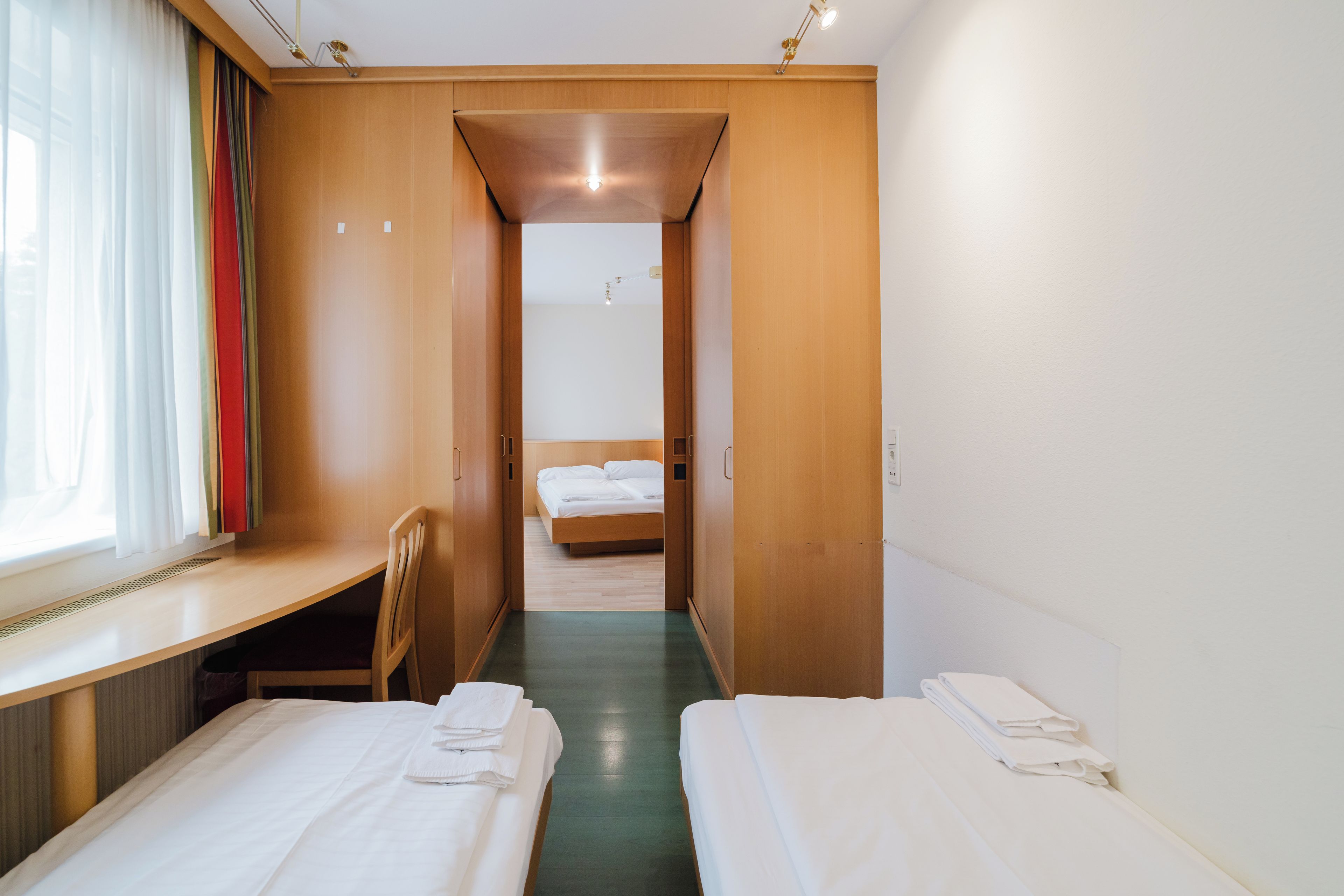 Una habitación de hotel con escritorio, dos camas y ventana con cortinas.