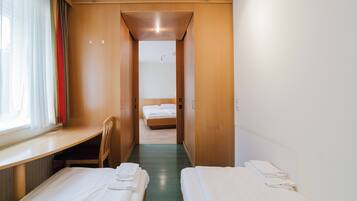 Una habitación de hotel con escritorio, dos camas y ventana con cortinas.
