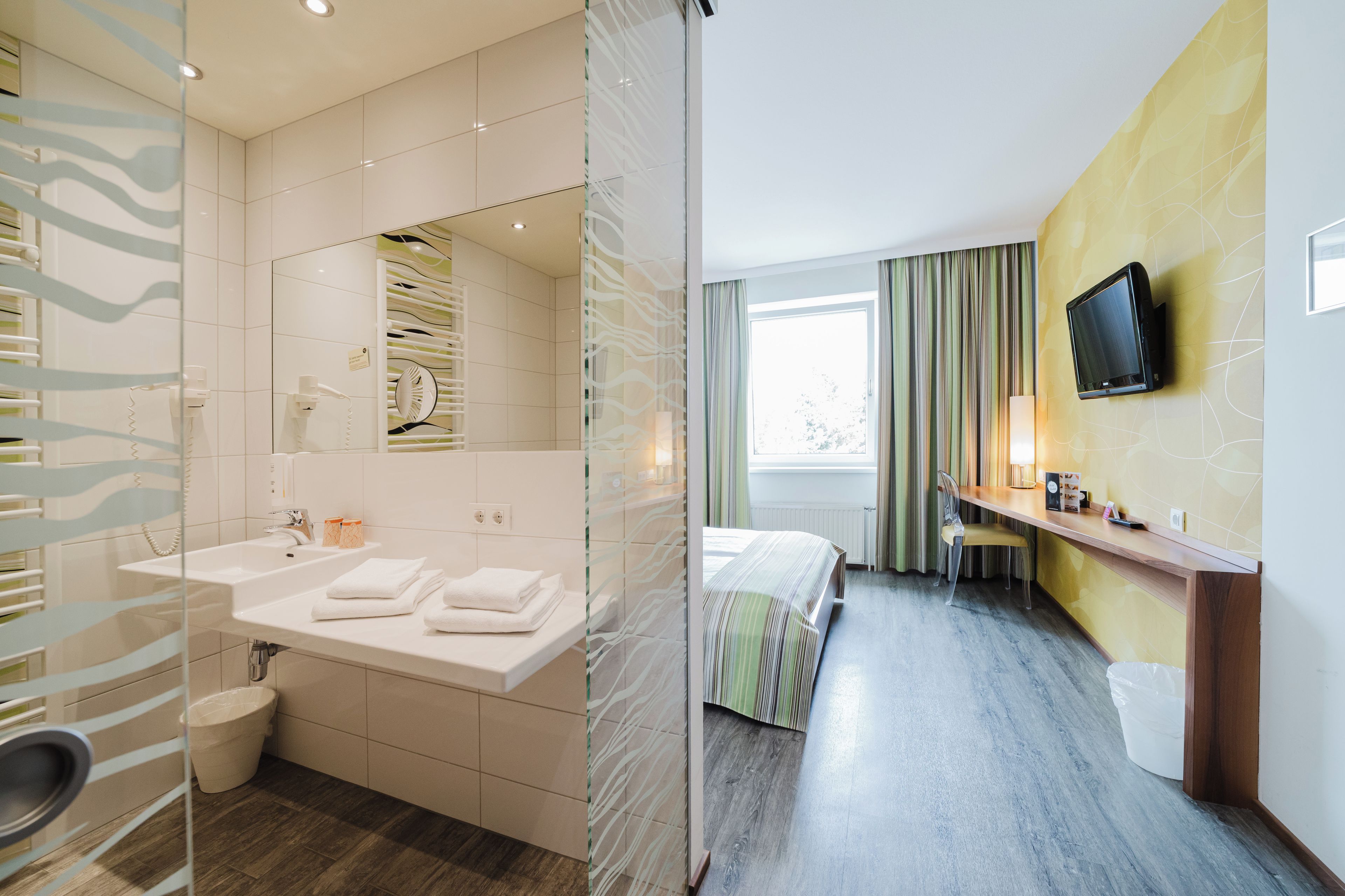 Habitación de hotel con baño, cama, escritorio y televisión.