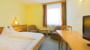 Een hotelkamer met een bed, een stoel, een klein tafeltje, een televisie en een raam met gordijnen.
