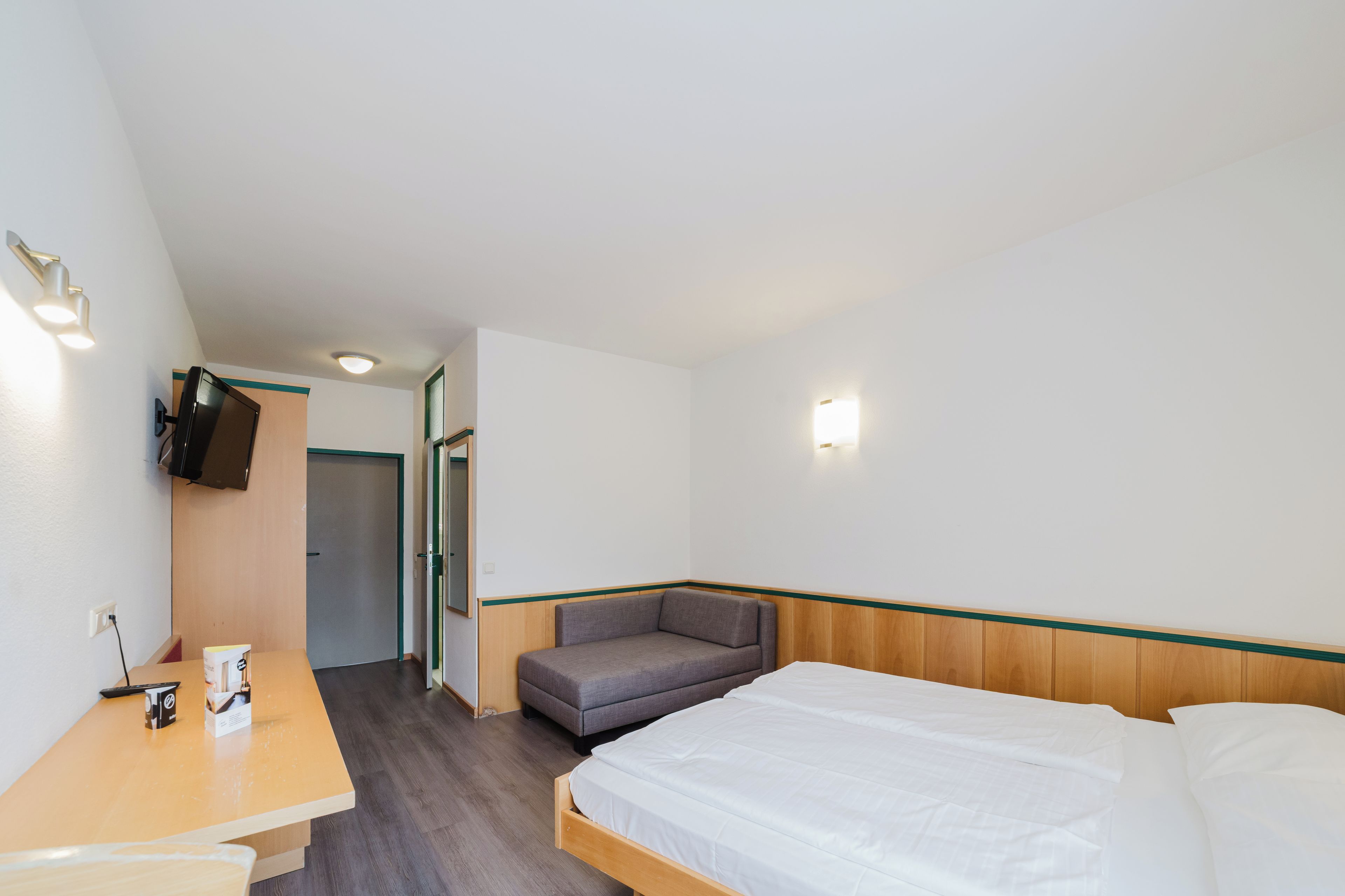 A hotel room with a bed, a desk, a chair, a television, and a door.