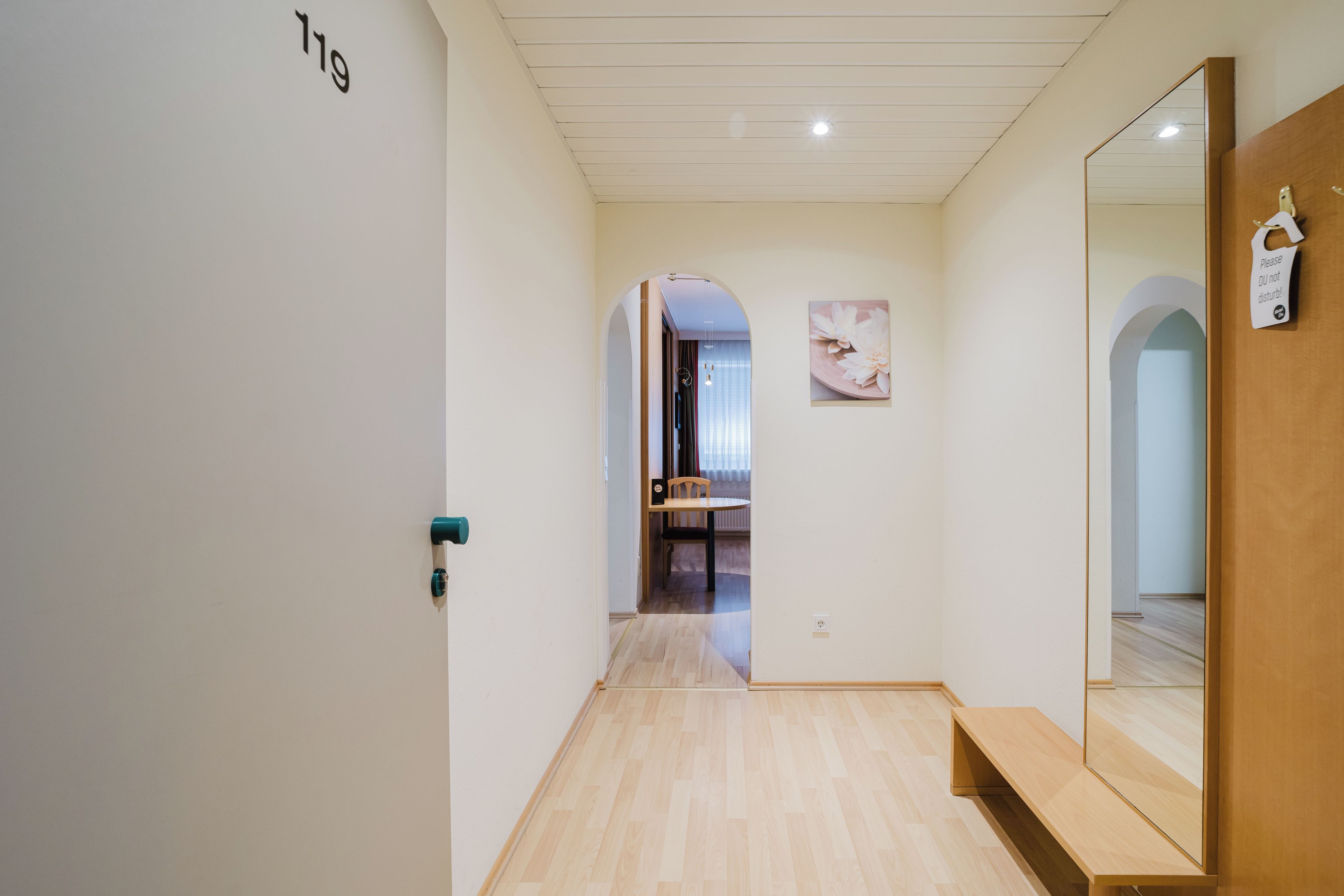 Ein Flur mit Holzboden, einer Tür mit Nummer, einem Spiegel und einem an der Wand befestigten Schild.